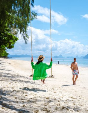 Plajda salıncakta sallanan bir kadın olan Phuket Tayland yakınlarındaki tropik Naka Adası plajında iki erkek ve bir kadın. Naka Adası Phuket Tayland