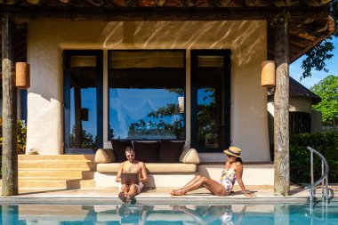 Men working at a laptop a digital nomad working at a swimming pool during a vacation on a tropical island. man and woman in the infinity pool during sunset. luxury vacation in a luxury pool villa