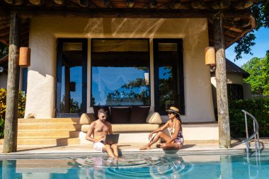 Men working at a laptop a digital nomad working at a swimming pool during a vacation on a tropical island. man and woman in the infinity pool during sunset. luxury vacation in a luxury pool villa