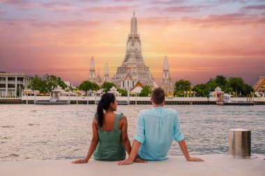 Tayland 'da gün batımında Bangkok' taki Wat Arun Tapınağı. Gün batımında Chao Praya Nehri. Bir çift adam ve bir kadın Bangkok Tayland 'a şehir gezisine gittiler. Nehir kenarında gün batımını izliyorlar.