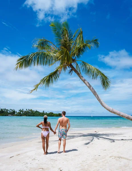 Tropik Koh Kood Adası veya Koh Kut Tayland. Tayland 'da tatilde olan birkaç erkek ve kadın ellerinde asılı bir palmiye ağacıyla sahilde yürüyorlar. Tatil adası Doğu Tayland Trang' da hoplayıp zıplıyorlar.