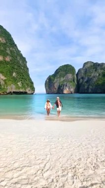 Taylandlı kadınlar ve şapkalı beyaz erkekler Koh Phi Phi Tayland 'da Maya Körfezi sahilinde yürüyorlar. Tayland' da tatilde olan çok ırklı, olgun bir çift.