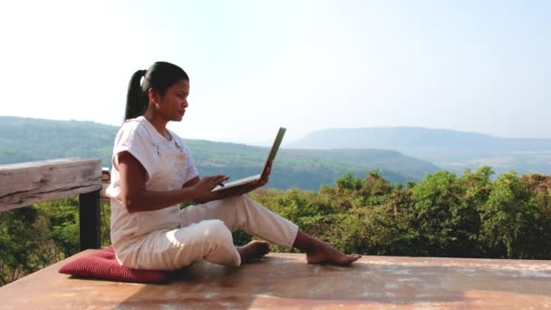 タイの山で日当たりの良い日に竹小屋の外に座っているラップトップを持つリモートオンライン作業デジタルノマド女性 モックアップを使用してビジネス女性 — ストック動画