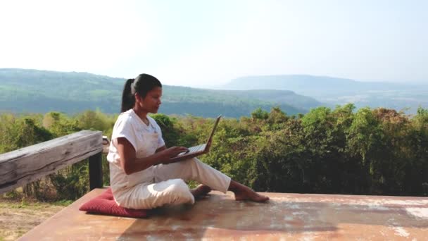 タイの山で日当たりの良い日に竹小屋の外に座っているラップトップを持つリモートオンライン作業デジタルノマド女性 モックアップを使用してビジネス女性 — ストック動画