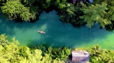 Koh Chang Tayland tropikal adasında kano süren bir çift kadın ve erkek, güneş batarken Koh Chang ormanındaki tropikal bir nehirde kano görüntüsü.