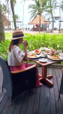 Plajda okyanus manzaralı lüks bir kahvaltı masası olan Asyalı kadın Koh Kood Tayland 'da. Ekmek, yumurta, kahve ve meyve suyu ile kahvaltı masası.