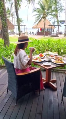 Plajda okyanus manzaralı lüks bir kahvaltı masası olan Asyalı kadın Koh Kood Tayland 'da. Ekmek, yumurta, kahve ve meyve suyu ile kahvaltı masası.