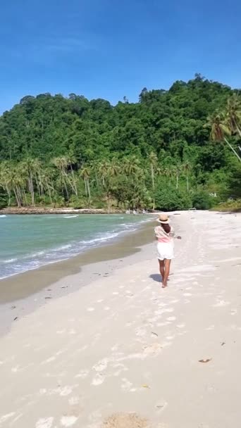 在一个阳光明媚的日子里 在泰国高库德岛的海滩上散步的亚洲妇女 在一个阳光明媚的日子里 泰国高库德岛是一个拥有棕榈树和草屋色海洋的热带海滩 — 图库视频影像