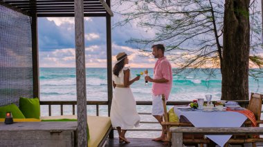 Koh Kood Tayland 'da kumsalda romantik bir akşam yemeği, orta yaşlı olgun bir çift ve Asyalı bir kadın ve Tayland sahilinde akşam yemeği yiyen Avrupalı bir erkek Ko Kut Trat' ta gün batımında.