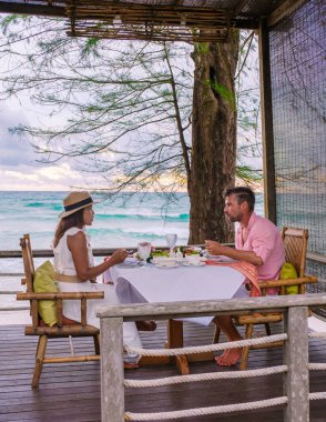 Koh Kood Tayland 'da kumsalda romantik bir akşam yemeği, orta yaşlı olgun bir çift ve Asyalı bir kadın ve Tayland sahilinde akşam yemeği yiyen Avrupalı bir erkek Ko Kut Trat' ta gün batımında.