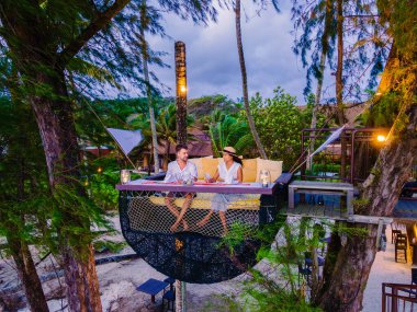 Koh Kood Tayland 'da kumsalda romantik bir akşam yemeği, Ko Kut Trat' ta gün batımında Tayland 'da bir kuş yuvasının tepesinde sahilde yemek yiyen bir çift erkek ve kadın.