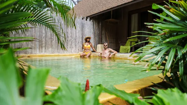 a couple of men and woman on a luxury vacation in Thailand at a 5 star resort relaxing in the swimming pool modern house with a swimming pool on a sunny day in the green jungle forest