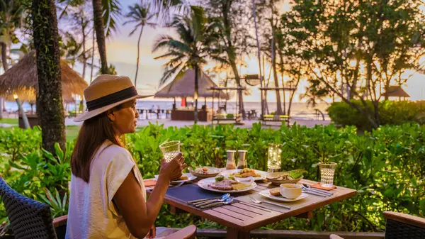 Romantic dinner on the beach in Koh Kood Thailand, woman watching sunset during dinner on the beach with a wooden pier and private patio on a luxury vacation in Thailand