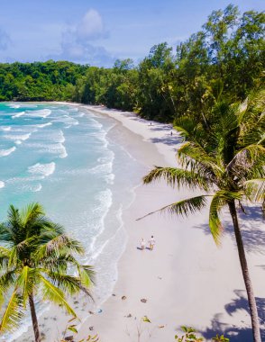 Ao Jark Körfezi ve Beach Koh Kood Adası Trat 'taki palmiye ağaçları, palmiye ağaçlarıyla tropik plajlar ve güneşli bir günde turkuaz renkli bir okyanus, Ko Kut sahilinde yürüyen bir çift. 