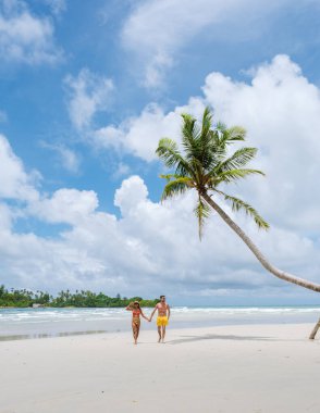 Gizli Kumsal Kood Adası Tayland Trat, güneşli bir günde, tropik bir plajda palmiye ağaçları ve turkuaz renkli bir okyanusta yürüyen birkaç erkek ve kadın.