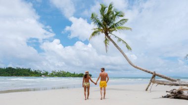 Koh Kood Adası Tayland Trat, güneşli bir günde, tropik bir plajda palmiye ağaçları ve turkuaz renkli bir okyanusta yürüyen birkaç erkek ve kadın.