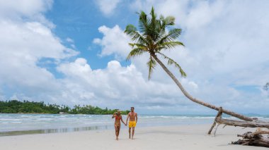 Gizli Sahil Koh Kood Adası Tayland Trat, güneşli bir günde, tropik bir plajda palmiye ağaçları ve turkuaz renkli bir okyanusta yürüyen birkaç erkek ve kadın.