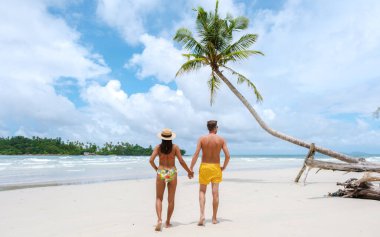 Gizli Kumsal Kood Adası Tayland Trat, güneşli bir günde, tropik bir plajda palmiye ağaçları ve turkuaz renkli bir okyanusta yürüyen birkaç erkek ve kadın.