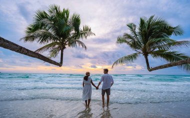 Koh Kood Adası Trat sahilinde gün batımını izleyen bir çift erkek ve kadın, palmiye ağaçları ve turkuaz renkli bir okyanus olan Ko Kut Adası tropikal plajı.
