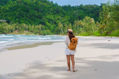 Sırt çantalı Asyalı bir kadın kumsalda Koh Kood Adası 'nda yürüyor Tayland Trat, tropik ada Ko Kut Adası sahilinde yürüyor hindistan cevizi palmiyeleri kumsalda, insansız hava aracı antenli.