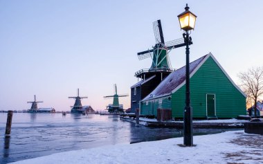 Güneş doğarken Zaanse Schans Hollanda 'da kar yağışlı bir Hollanda yel değirmeni köyü