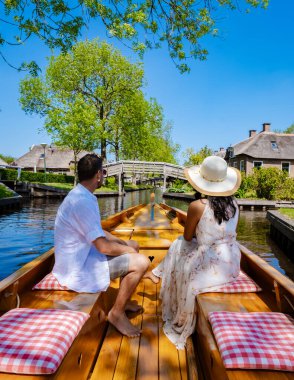 Çift Giethoorn Hollandalı çifti, Avrupa 'da sıcak bir bahar gününde bir çiftlikte, kanalı ve sazdan çatı evlerini gören ünlü köy manzaralı bir tekneyle köyü ziyaret ediyor.