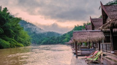 Tayland 'da Kwai nehri kıyısındaki tropik sahil evleri. Gün batımında Kwai Kanchanaburi nehrinde yüzen bir sal evi.