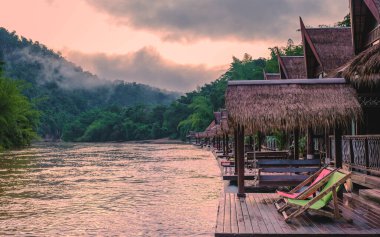 Tayland 'da Kwai nehri kıyısındaki tropik sahil evleri. Yağmur mevsiminde Kwai Kanchanaburi nehrinde yüzen sal evi.