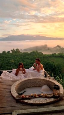 Erkekler ve kadınlar bir küvette tatil sırasında Kuzey Tayland dağlarına bakıyorlar. Gün batımında sisli ve sisli dağlarda açık banyo ve küvet.