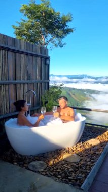 Bir küvette iki erkek ve kadın tatil sırasında Chiang Rai Kuzey Tayland dağlarına bakıyorlar. Açık banyo, gün batımında Doi Chang dağında sisli ve sisli bir küvet.