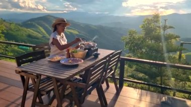 Kuzey Tayland 'da tatilde olan Asyalı kadınlar, Chiang Rai Doi Chang dağlarında bir kulübede kalıyorlar ve Tayland barbeküsüyle yemek yiyorlar.
