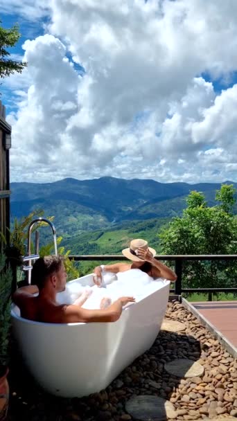 バスタブにいた男女2人が 休暇中に チェンライ北部のタイの山々を 眺めていました ドイチャン山のバスタブ付きテラスの屋外バスルーム — ストック動画