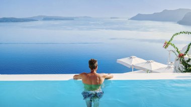 Yüzme şortlu genç bir adam havuzda dinleniyor Santorini Adası Yunanistan 'ın kalderasına bakıyor, sonsuz havuzda bir adam, Avrupa' da lüks bir tatilde olan genç bir adam Yunanistan 'da.