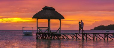 Erkek ve kadın, Mauritius 'ta tropik bir plajda okyanusta gün batımını seyrediyor. Bir çift de Mauritius' ta balayı tatilinde.