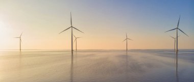 Günbatımında okyanusta yel değirmeni parkı, yeşil enerji üreten yel değirmeni türbinlerinin insansız hava görüntüsü, Hollanda 'da denizde izole edilmiş yel değirmenleri.. 