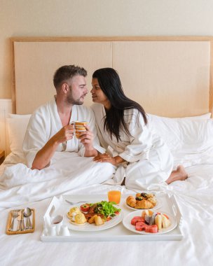 Çift yatakta kahvaltı yapıyor, erkek ve kadın yatak odasında sabah kahvaltı yapıyor. Kahve ve meyve ile, yatakta romantik bir an.