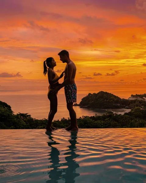 a couple of European men and an Asian woman in an infinity pool in Thailand looking out over the ocean, a luxury vacation in Thailand Koh Lanta Island at sunset