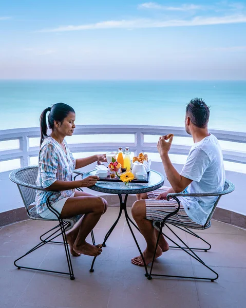 couple having breakfast on the balcony looking out over the ocean, an Asian woman and European man on vacation in Thailand Pattaya Asia