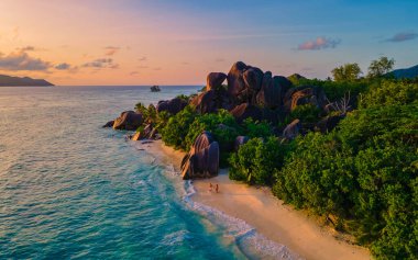 Anse Source dArgent plajı, La Digue Adası, Seyşeller, yukarıdan bir çift erkek ve kadının gün batımında Seyşeller 'de lüks bir tatilde kumsalda yürüyüşü.