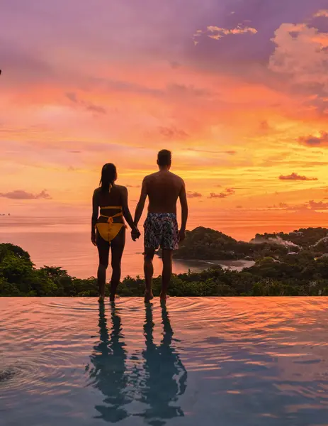Romantic couple of men and women at a swimming pool during a vacation on a tropical island. man and woman in the infinity pool during sunset. luxury vacation in a luxury pool villa during the summer