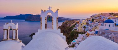 Santorini Yunanistan, Beyaz kiliseler ve güneş batarken Santorini 'deki geleneksel bir Yunan köyü olan Oia Santorini Yunanistan' ın okyanus kıyısındaki mavi kubbeler