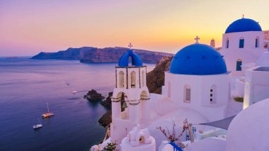 Santorini Yunanistan, Beyaz kiliseler ve güneş batarken Santorini 'deki geleneksel bir Yunan köyü olan Oia Santorini Yunanistan' ın okyanus kıyısındaki mavi kubbeler. Yunan yaz tatilleri Avrupa