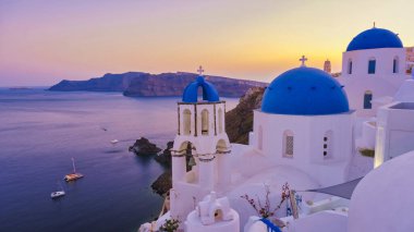 Santorini Yunanistan, Beyaz kiliseler ve güneş batarken Santorini 'deki geleneksel bir Yunan köyü olan Oia Santorini Yunanistan' ın okyanus kıyısındaki mavi kubbeler. Yunan yaz tatilleri Avrupa