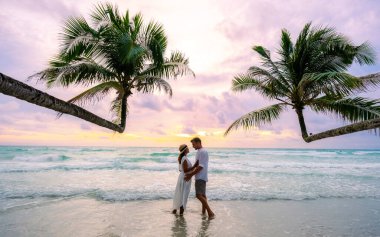 Bir çift erkek ve kadın gün batımını izliyor ve Koh Kood Adası Tayland Trat sahilinde sarılıyorlar. Palmiye ağaçları ve turkuaz renkli bir okyanus olan Ko Kut Adası 'nda.