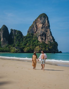 Railay Beach Krabi Tayland plajında yürüyen iki erkek ve kadın, Railay Krabi 'nin tropikal plajı, tatilde el ele yürüyen çok ırklı bir çift.