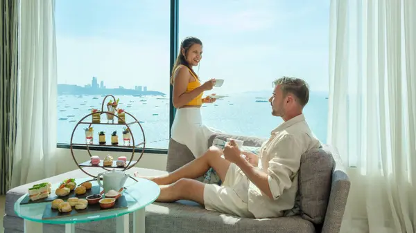 A couple of men and woman having afternoon tea or high tea in a hotel room with bright fresh colors, a minimal style bedroom with an ocean view in Pattaya Thailand