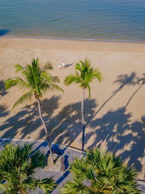 Pattaya Tayland plaj yolunda palmiye ağaçlarıyla sahilde yürüyen bir çift kadın ve erkeğin uzaktan kumandalı görüntüsü.