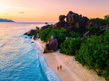 Anse Source d 'Argent plajı, La Digue Adası, Seyşeller, İHA hava görüntüsü La Digue Seyşeller, gün batımında lüks bir tatilde gün batımında sahilde yürüyen çift erkek ve kadın.
