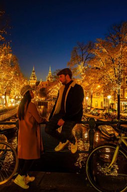 Amsterdam Hollanda 'da Aralık ayı boyunca Noel ışıkları, gece de Amsterdam' ın kanal tarihi merkezi bulunuyor. Bir çift erkek ve bir kadın kış boyunca şehir gezisinde.