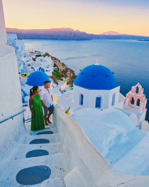 Yunanistan 'da yaz tatilinde Santorini' de gün batımını izleyen çift, Yunanistan 'da beyaz kiliseli ve mavi kubbeli köyü izleyen erkekler ve kadınlar